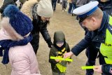 Funkcjonariusz Policji przekazuje dziecku żółtą opaskę odblaskową.