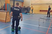 Fotografia kolorowa. Policjanci na sali gimnastycznej przeprowadzają test sportowy dla młodzieży.