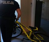 Na zdjęciu widać funkcjonariusza stojącego tyłem trzymającego żółty rower. Zdjęcie robione jest w pomieszczeniu
