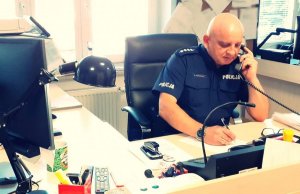 Na zdjęciu widać rozmawiającego przez telefon policjanta na stanowisku kierowania