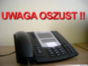 Czarny telefon stacjonarny z przyciskami . nad telefonem napis UWAGA OSZUST!!!