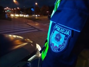 Emblemat Komendy Miejskiej Policji w Łomży na mundurze policyjnym. Emblemat na przedramieniu policjanta, który stoi przy jezdni.
