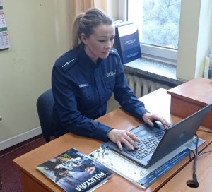 Policjantka pisząca na klawiaturze komputera w pokoju służbowym, przeprowadza spotkanie online z uczniami.