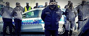 Radiowóz policyjny otoczony grupą umundurowanych policjantów. Zdjęcie za dziedzińcu komendy.