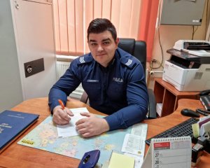 Umundurowany policjant siedzący za biurkiem w pokoju służbowym.