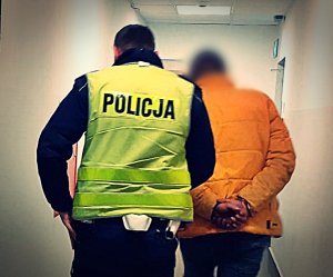 Policjant Wydziału Ruchu Drogowego prowadzi mężczyznę przez korytarz