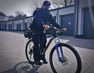 Zdjęcie na dziedzińcu komendy, policjant w mundurze na rowerze służbowym
