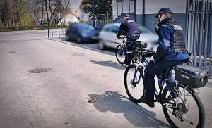 Dwóch policjantów na rowerach służbowych wyjeżdżający przez bramę komendy w kierunku parku