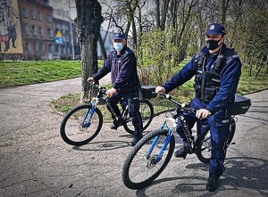 Dwóch policjantów na rowerach służbowych stojący na skraju parku