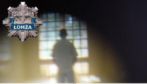 Młody mężczyzna stojący w półmroku odwrócony twarzą do okna tyłem do obiektywu. W lewym górnym rogu gwiazda policyjna z napisem POLICJA ŁOMŻA