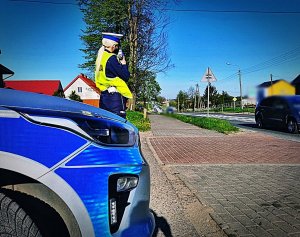 Policjantka stojąca przy radiowozie z ręcznym miernikiem prędkości