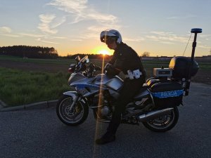 Policjant siedzący na motocyklu, w tle zachód słońca.