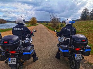 Dwóch policjantów na motocyklach, stoją na jezdni. Zdjęcie wykonano z tyłu jednośladu.