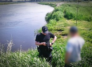 Policjant kontrolujący wędkarza nad brzegiem rzeki