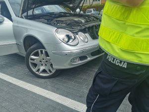 Spodnie służbowe z napisem policja i w tle kontrolowany samochód, który ma pękniętą lampę przednią.