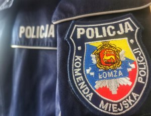 Emblemat Komendy Miejskiej Policji w Łomży i w oddali napis Policja na kurtce służbowej.