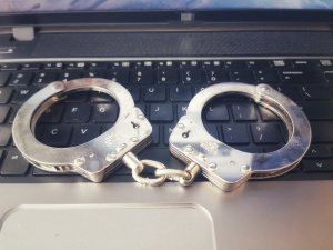 Policyjne kajdanki leżące na klawiaturze od komputera.