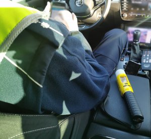 Policjant siedzący w radiowozie, sprawdza kierowcę w policyjnym systemie. Obok leży alcoblow- urządzenie do badania stanu trzeźwości.