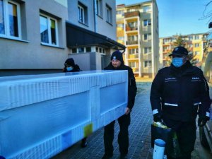 Policjanci wnoszą lodówkę do mieszkania w bloku.