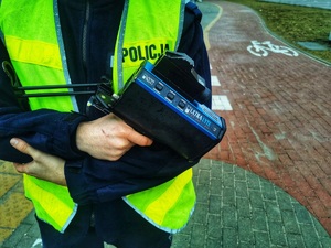 Umundurowany policjant trzyma w ręku ręczny miernik prędkości.