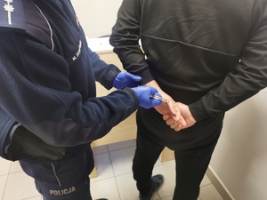 Umundurowany policjant zakłada kajdanki zatrzymanemu mężczyźnie