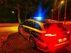 Oznakowany radiowóz policyjny w nocy stoi zaparkowany przy ulicy.