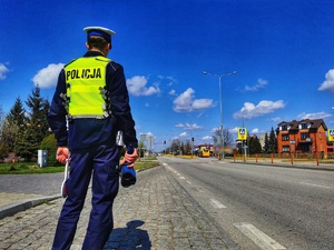 Umundurowany policjant stoi przy jezdni i trzyma ręczny miernik prędkości