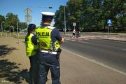 Dwoje policjantów stoi przy jezdni i przygląda się na zachowanie uczestników ruchu drogowego w okolicach przejścia dla pieszych