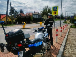 Policjant stoi obok służbowego motocykla w pobliżu oznakowanego przejścia dla pieszych.