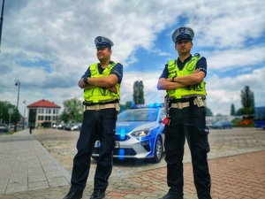 Dwóch umundurowanych policjantów stojących przy radiowozie