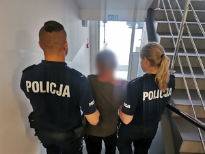 Dwójka policjantów prowadzi zatrzymanego mężczyznę schodami w komendzie.