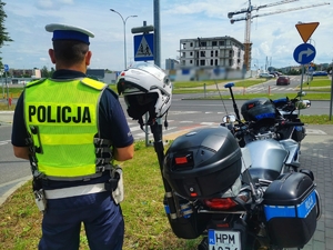 Policjant stoi obok motocykla przy przejściu dla pieszych.