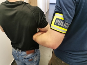 Policjant w ubraniu cywilnym z opaską na ręku z napisem policja trzyma zatrzymanego mężczyznę.