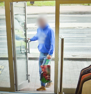 Mężczyzna w niebieskiej bluzie wchodzi do sklepu z torbą w ręku. Zdjęcie z monitoringu sklepu.