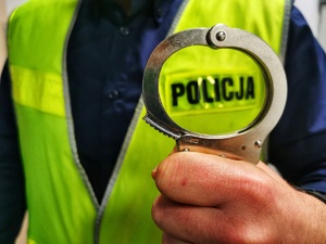 Policjant w kamizelce odblaskowej z napisem policja trzyma w ręku kajdanki