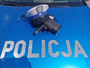 Pokrywa silnika radiowozu z napisem policja i8 nad nim czapka policyjna i ręczny miernik prędkości