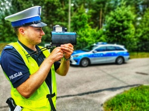 Umundurowany policjant mierzy prędkość jadącym pojazdom.
