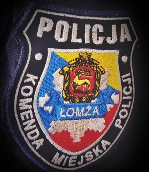 Granatowa Naszywka policyjna z napisem POLICJA , Komenda Miejska Policji, w środku na żółto -niebiesko-czerwonym tle herb Łomży i gwiazda policyjna