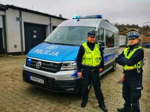 Dwóch umundurowanych policjantów stoi przy nowym radiowozie marki Volkswagen