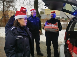 Policjanci w czapkach Mikołaja wyjmują z radiowozu prezenty dla dzieci.