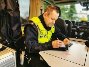 Policjant siedzi w radiowozie i pisze w notatniku służbowym
