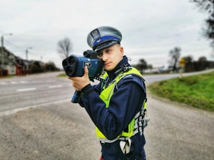 Policjant z ręcznym miernikiem prędkości prowadzi pomiar prędkości jadącym pojazdom